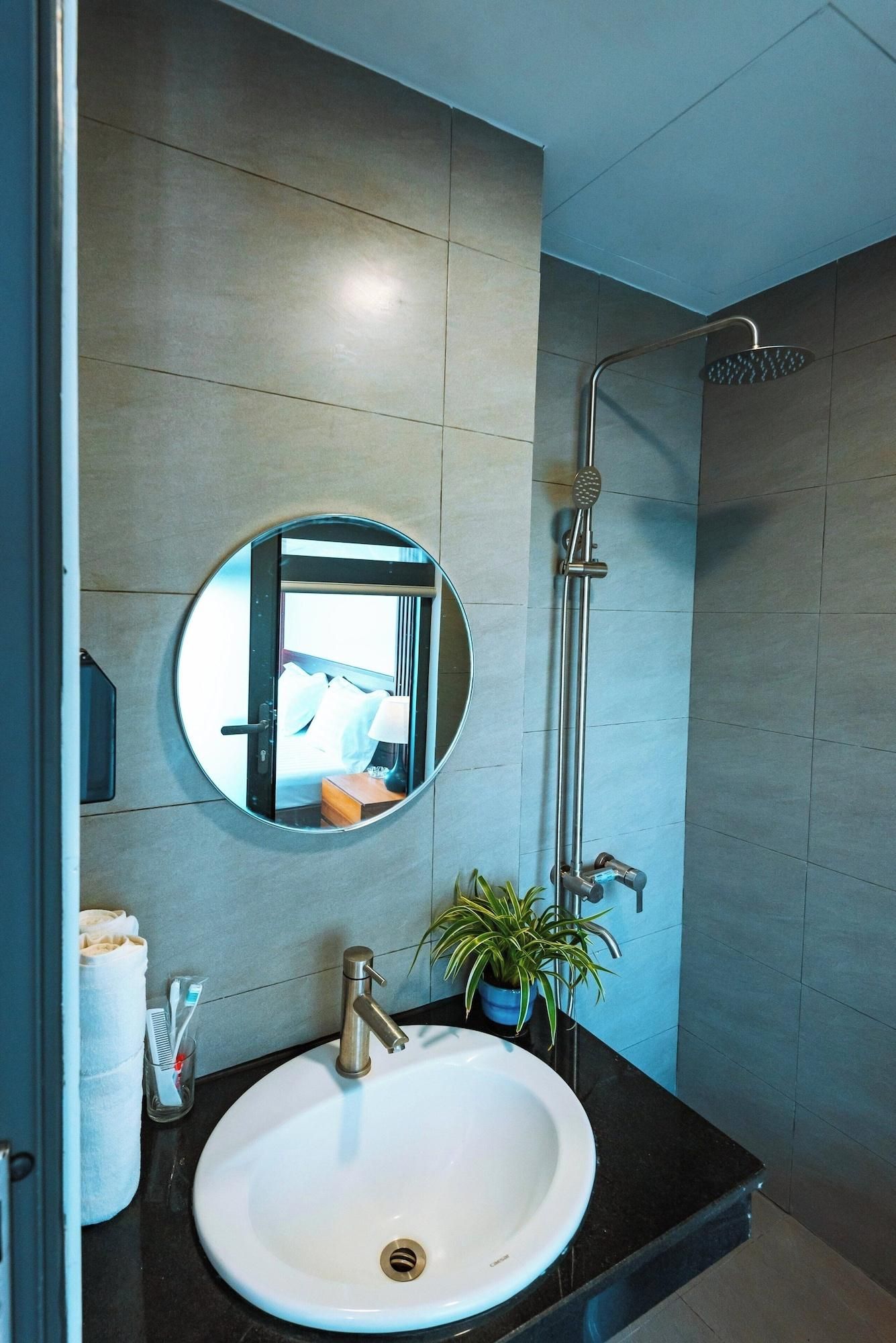 A modern bathroom with a round mirror, a sink, a shower, and a potted plant.