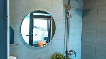 A modern bathroom with a round mirror, a sink, a shower, and a potted plant.