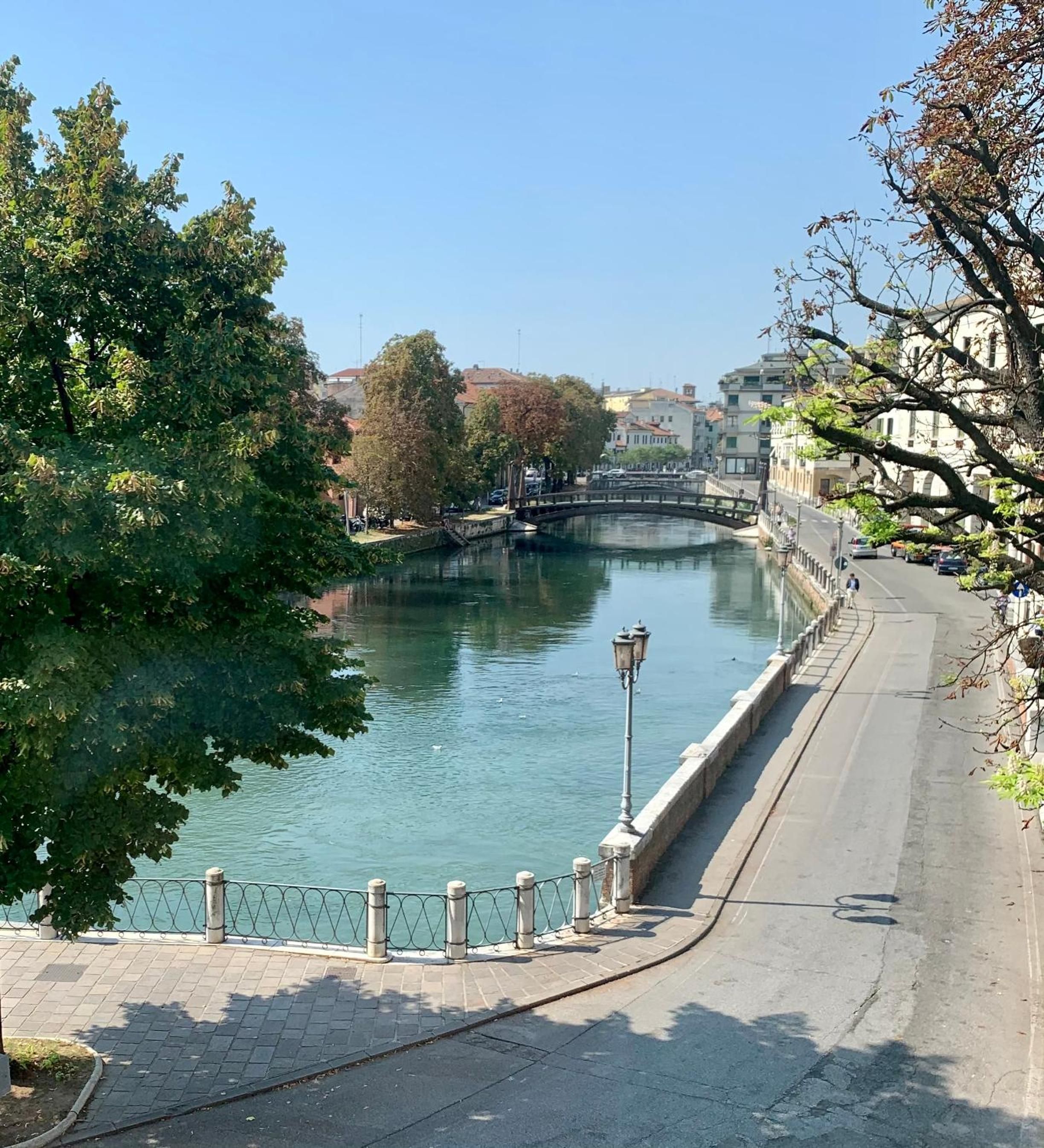 A riverside walkway with a paved path, a metal railing, and a bridge in the distance. - Locanda Ponte Dante (Treviso)