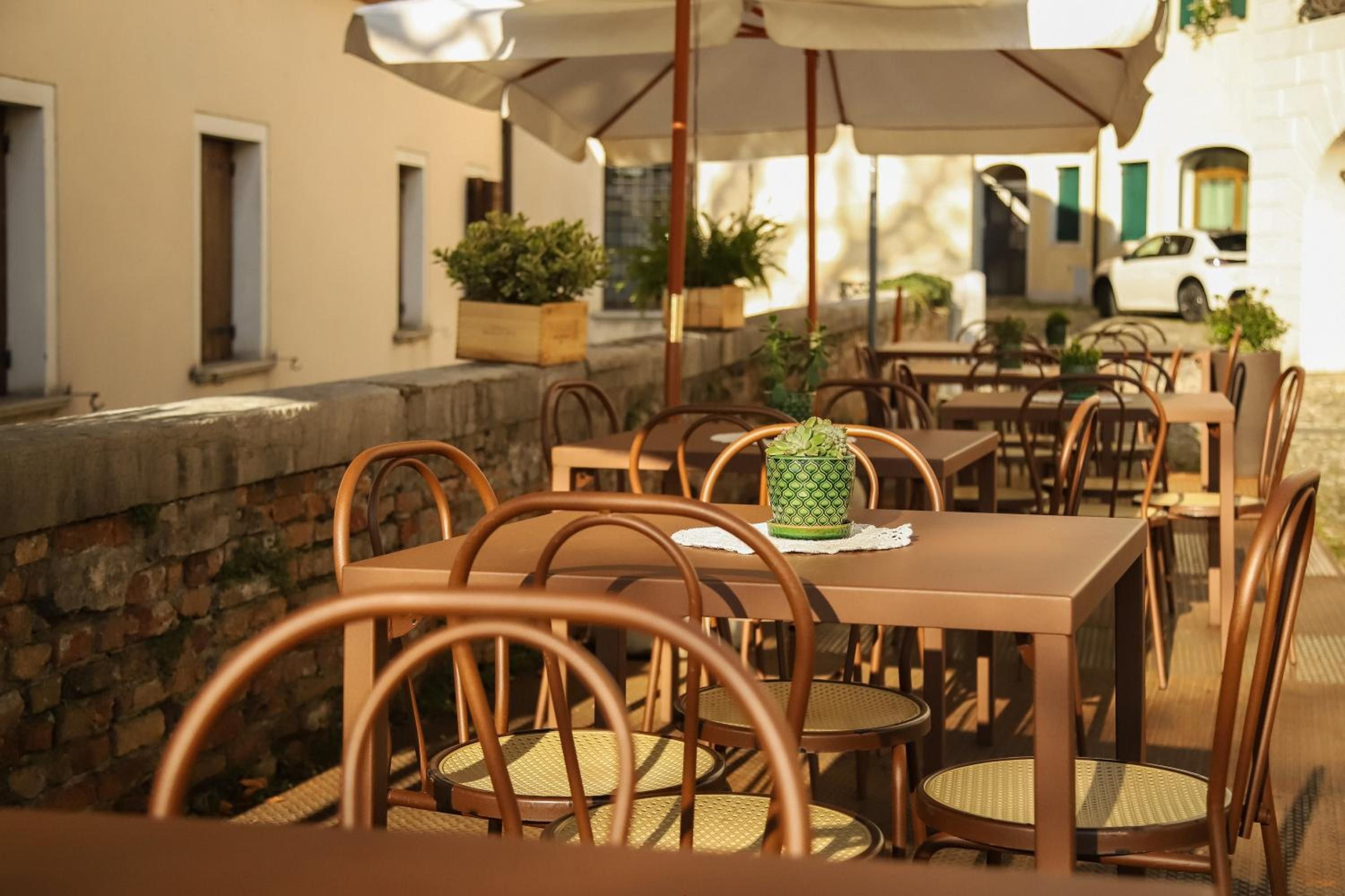 Un café en plein air avec des tables et des chaises, des plantes en pot et un mur en pierre.