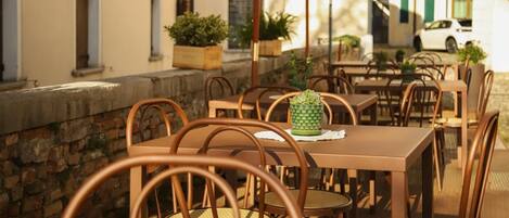 An outdoor cafe with tables and chairs, potted plants, and a stone wall.