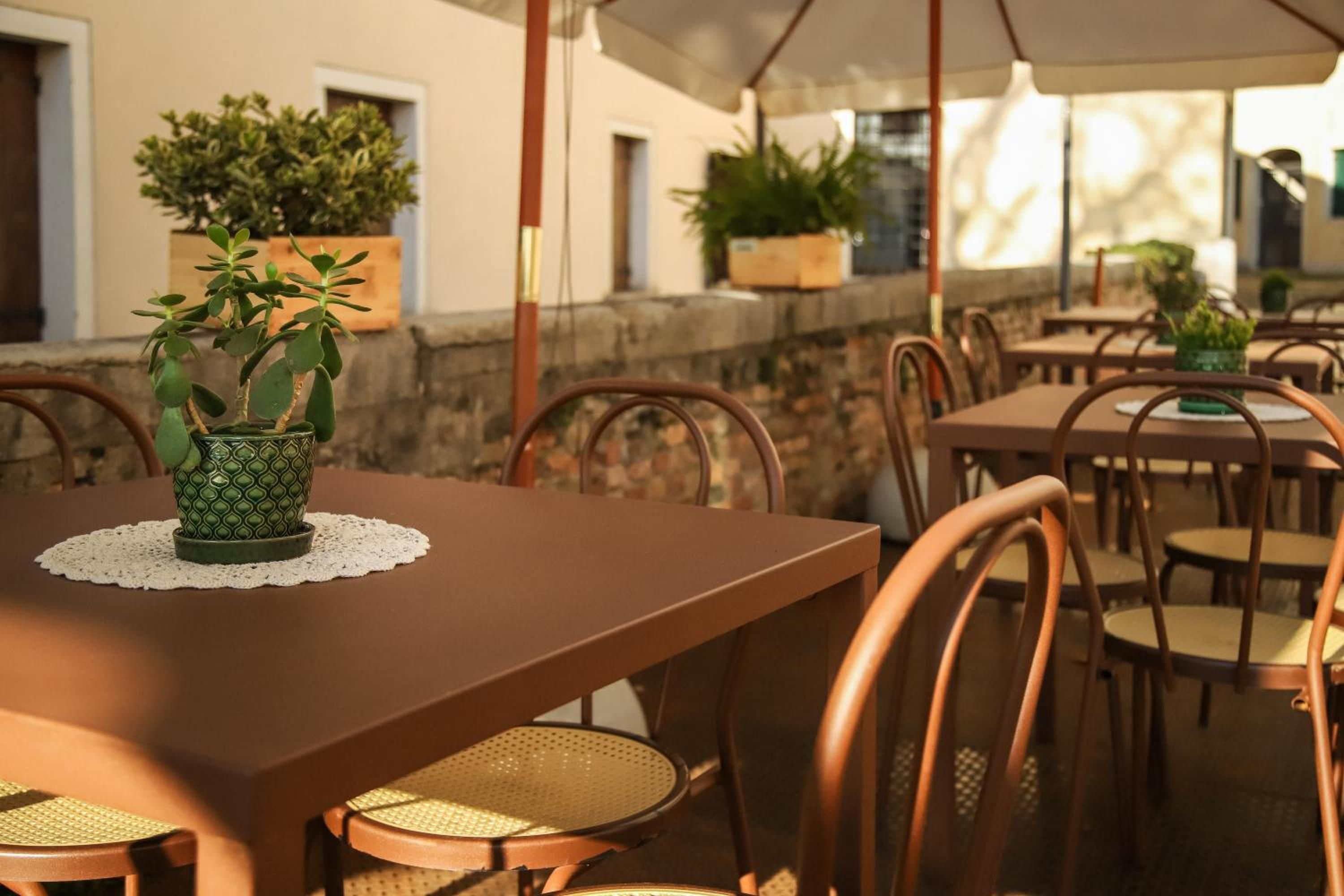 An outdoor dining area with tables and chairs, potted plants, and a stone wall.