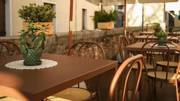 Zona pranzo all'aperto con tavoli e sedie, piante in vaso e un muro in pietra.