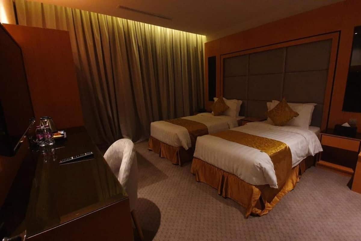 A hotel room with two beds, a desk, a chair, a nightstand, and a mirror.