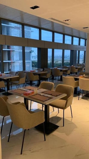 A modern dining area with tables and chairs, large windows, and a view of the cityscape. - Al Rayan Hotel (Jeddah)