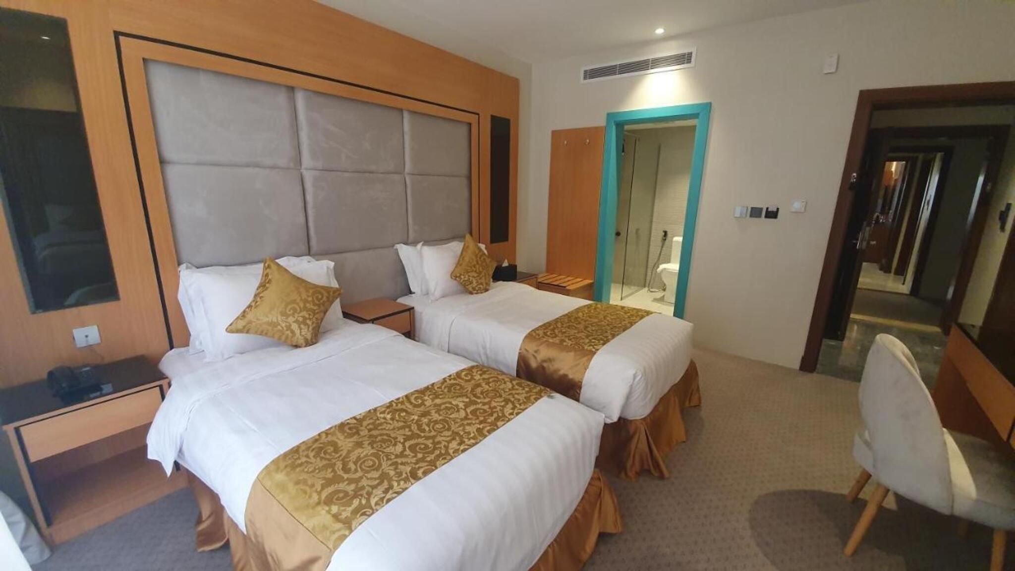 Habitación de hotel con dos camas, un escritorio, una silla y un baño visible a través de una puerta abierta.
