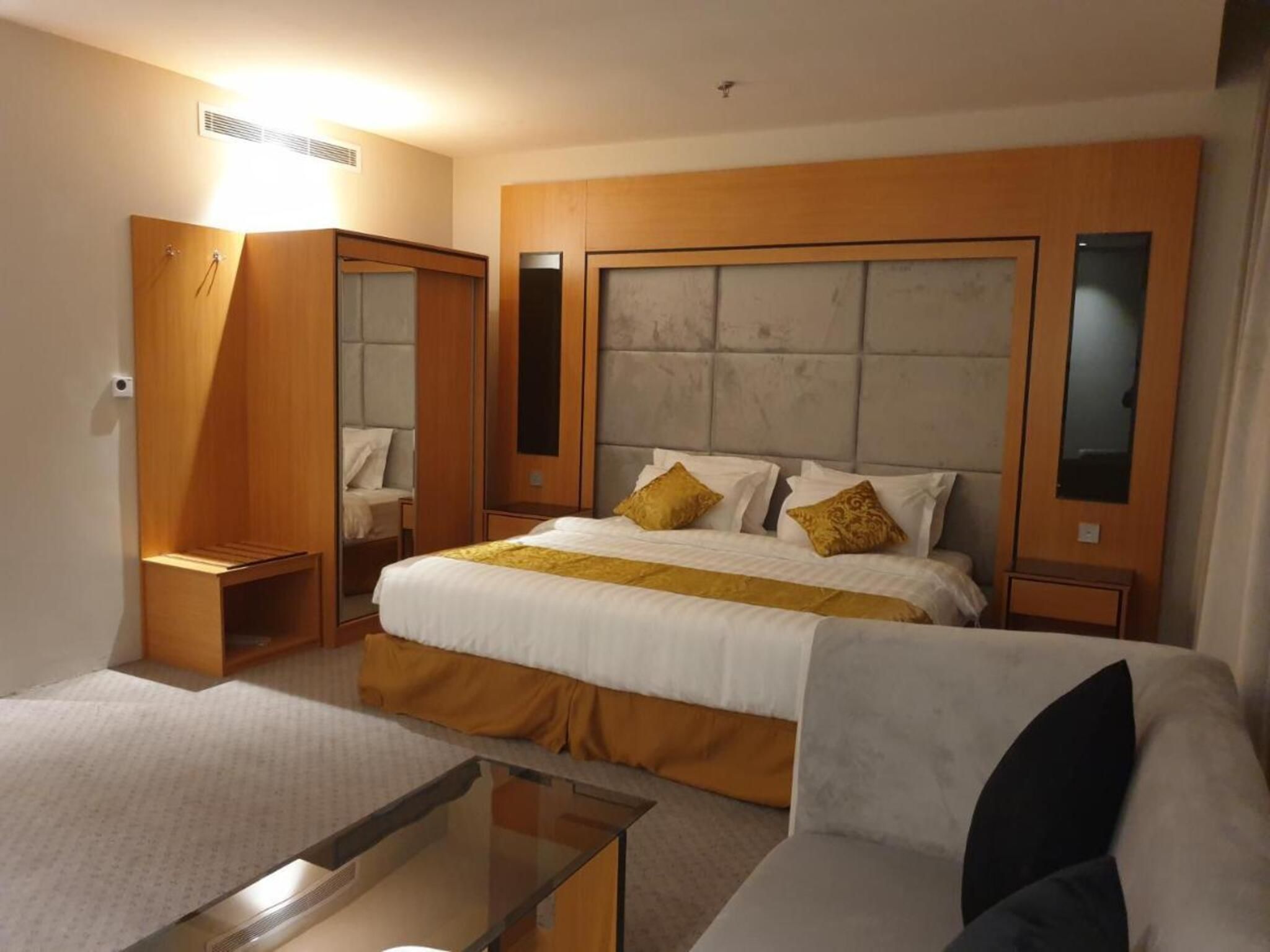 Ein Hotelzimmer mit einem großen Bett, einem Schlafsofa, einem Glastisch, einem Kleiderschrank und einem Spiegel.