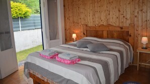 Quarto com cabeceira de madeira, cama com roupa de cama listrada, duas luminárias de cabeceira e vista para área externa cercada.