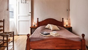 Uma cama de madeira com dossel, um painel de cabeceira, duas luminárias de mesa e uma toalha dobrada sobre a cama.