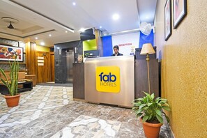 A reception area with a reception desk labeled 'fab hotels,' a reception counter, a wall-mounted fan, and a potted plant. - Fabhotel Royal Lagoon (Bhubaneshwar)