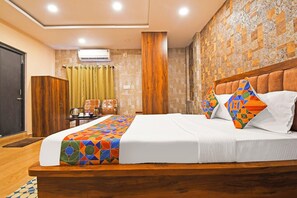 A hotel room with a large bed, a wooden headboard, a small table with a kettle, and a curtain. - Fabhotel Royal Lagoon (Bhubaneshwar)