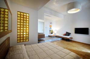 Un dormitorio moderno con cama, televisor, banco de madera y un panel decorativo en la pared.