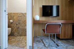 Un baño con inodoro, ducha y televisor montado en la pared.
