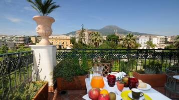 Un balcone con tavolo apparecchiato per la colazione, vista su una montagna e edifici circostanti.