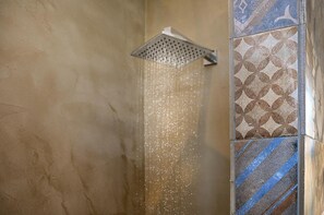 A shower with a square head, water flowing down, and a tiled wall with a geometric pattern. - Villa Battista (Ercolano)