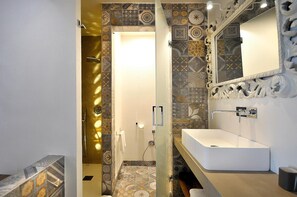 Baño con un espejo grande, un lavamanos y baldosas estampadas.