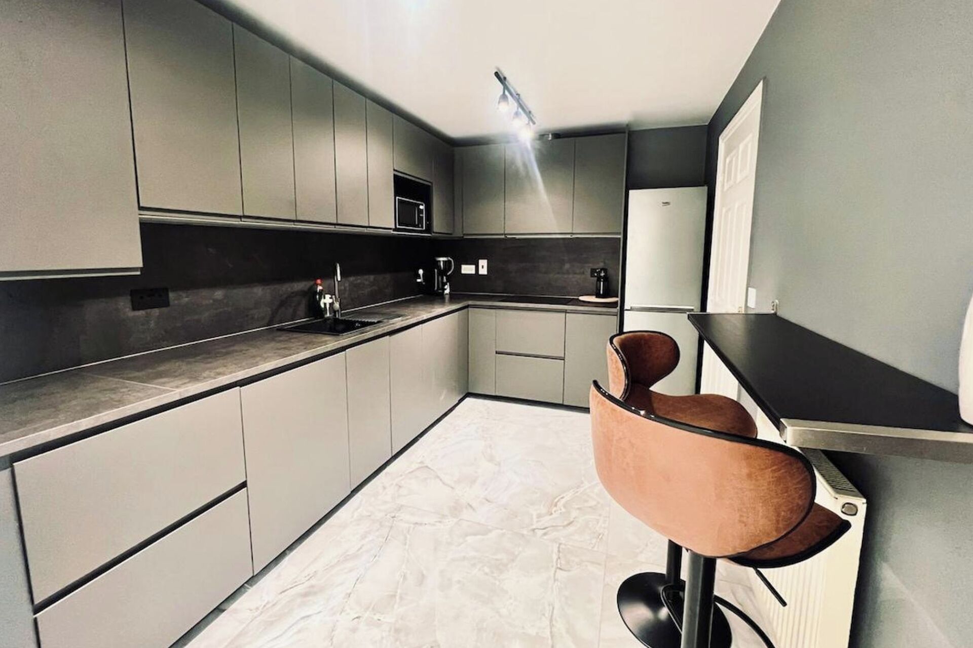 A modern kitchen with grey cabinets, a black countertop, and a bar area with a stool.