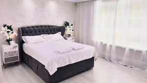 Un dormitori modern amb un llit gran, roba de llit blanca i dues tauletes de nit amb làmpades.