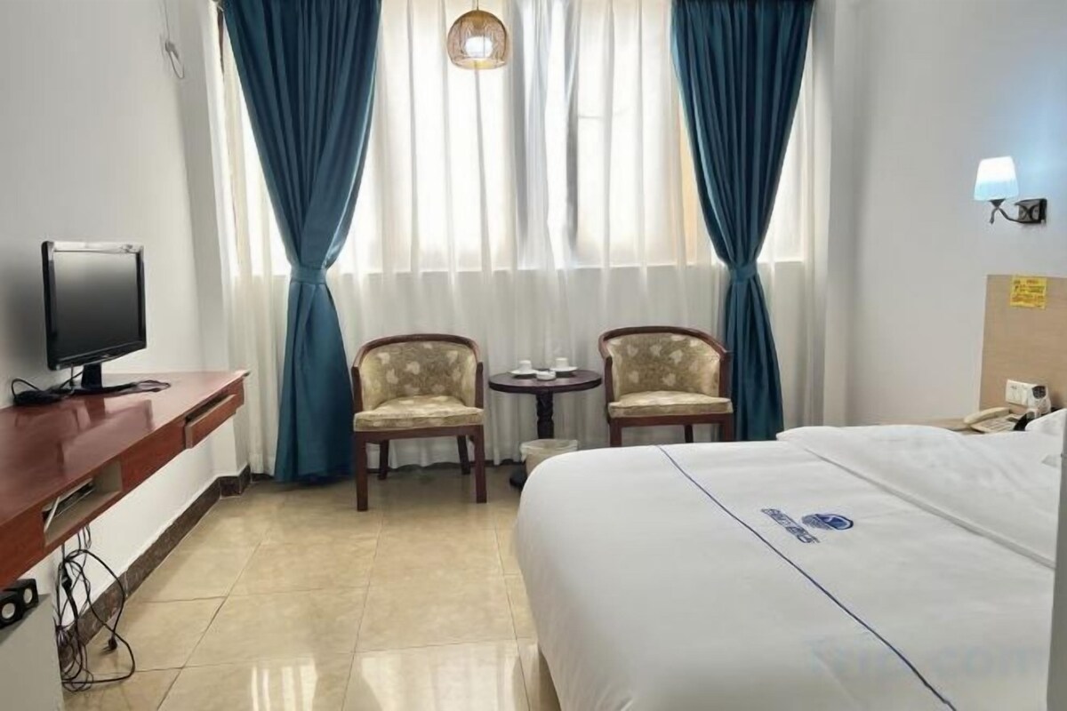 A hotel room with a bed, a desk with a television, two armchairs, a small table, and curtains.