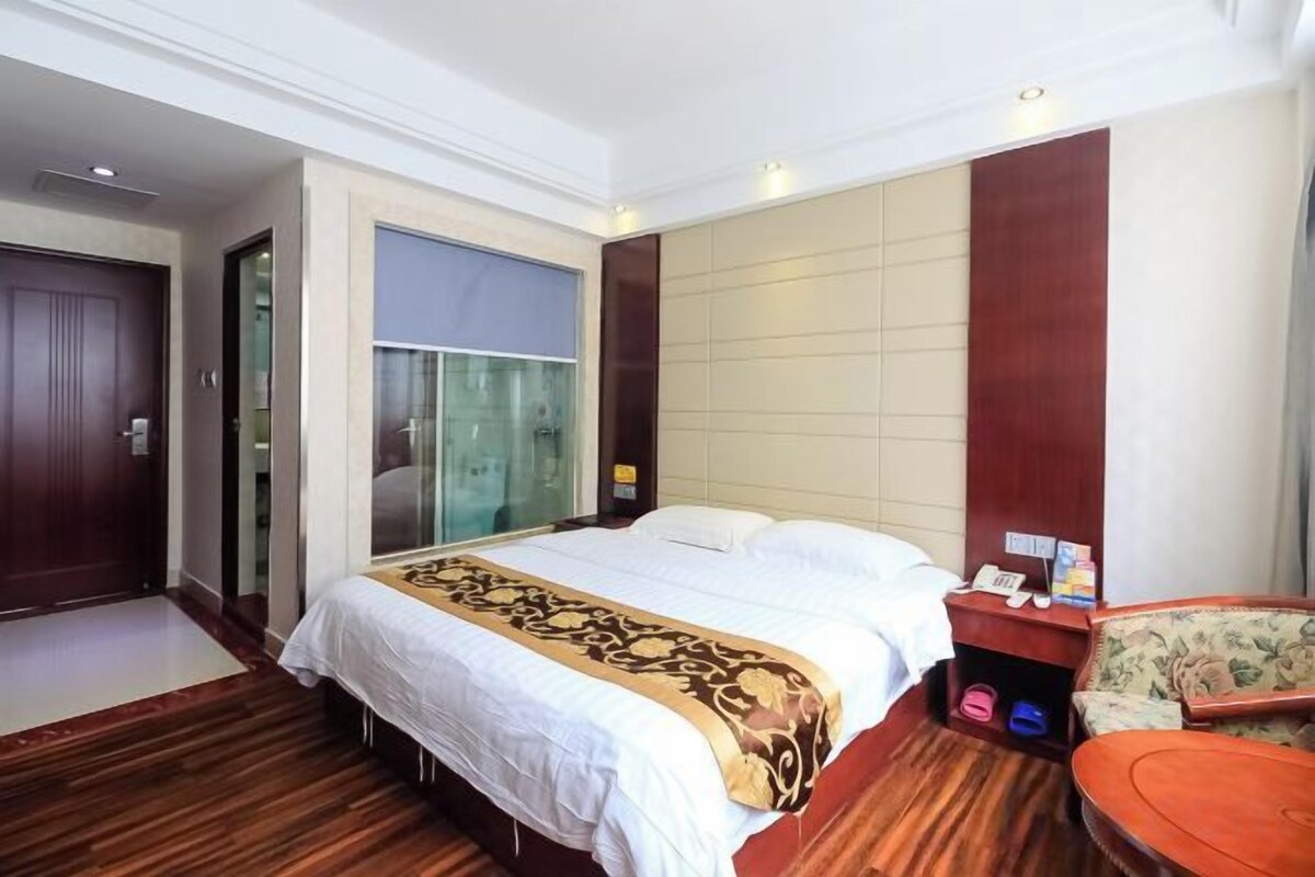 A hotel room with a large bed, a wooden floor, a seating area with a chair, and a small table.