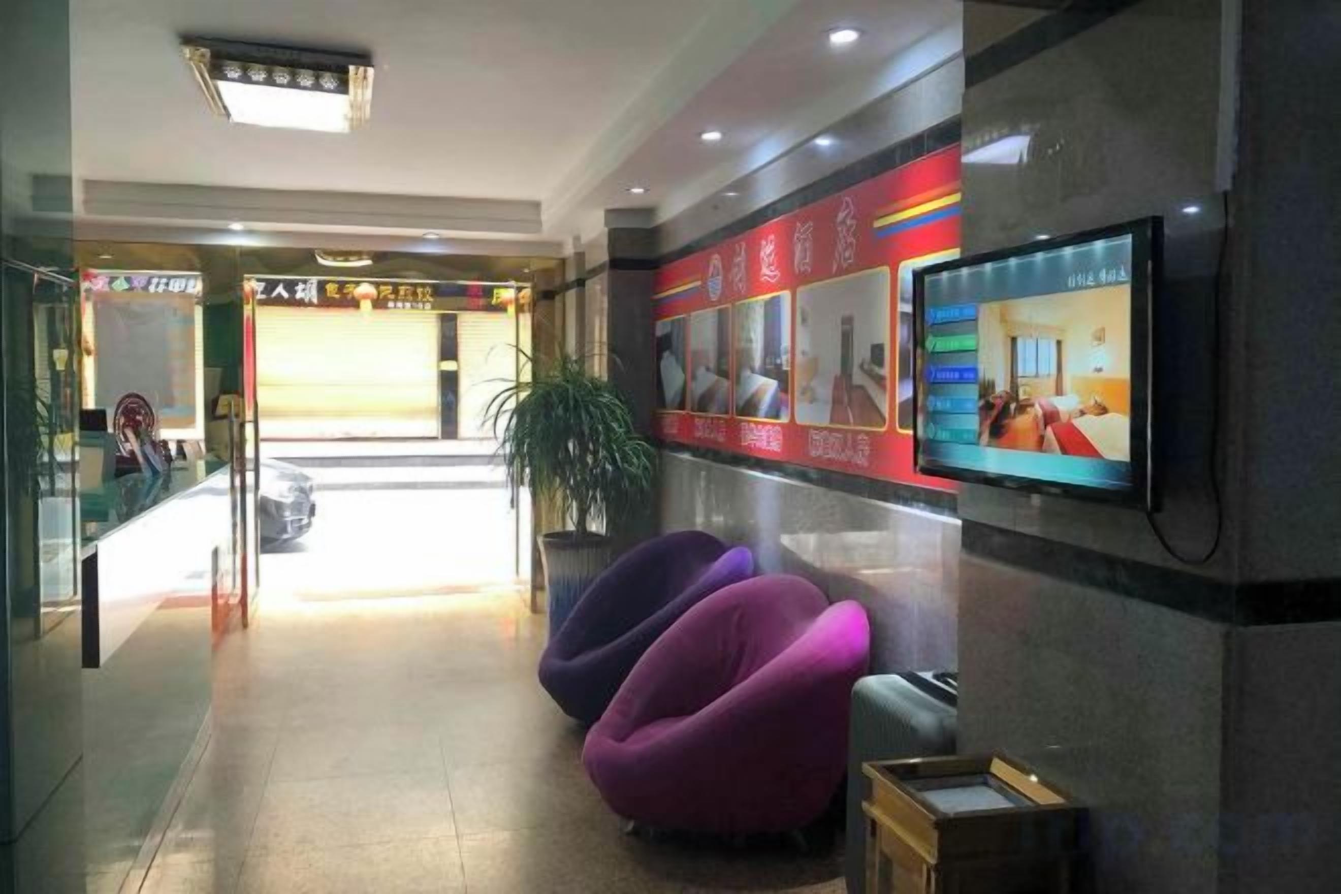 A hotel lobby with a reception desk, seating area, and a television screen.