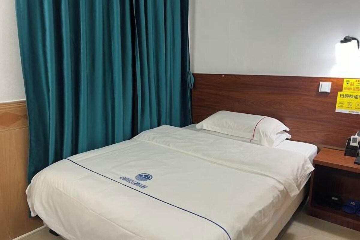 A hotel room with a bed, a nightstand, a lamp, and a sign on the wall.