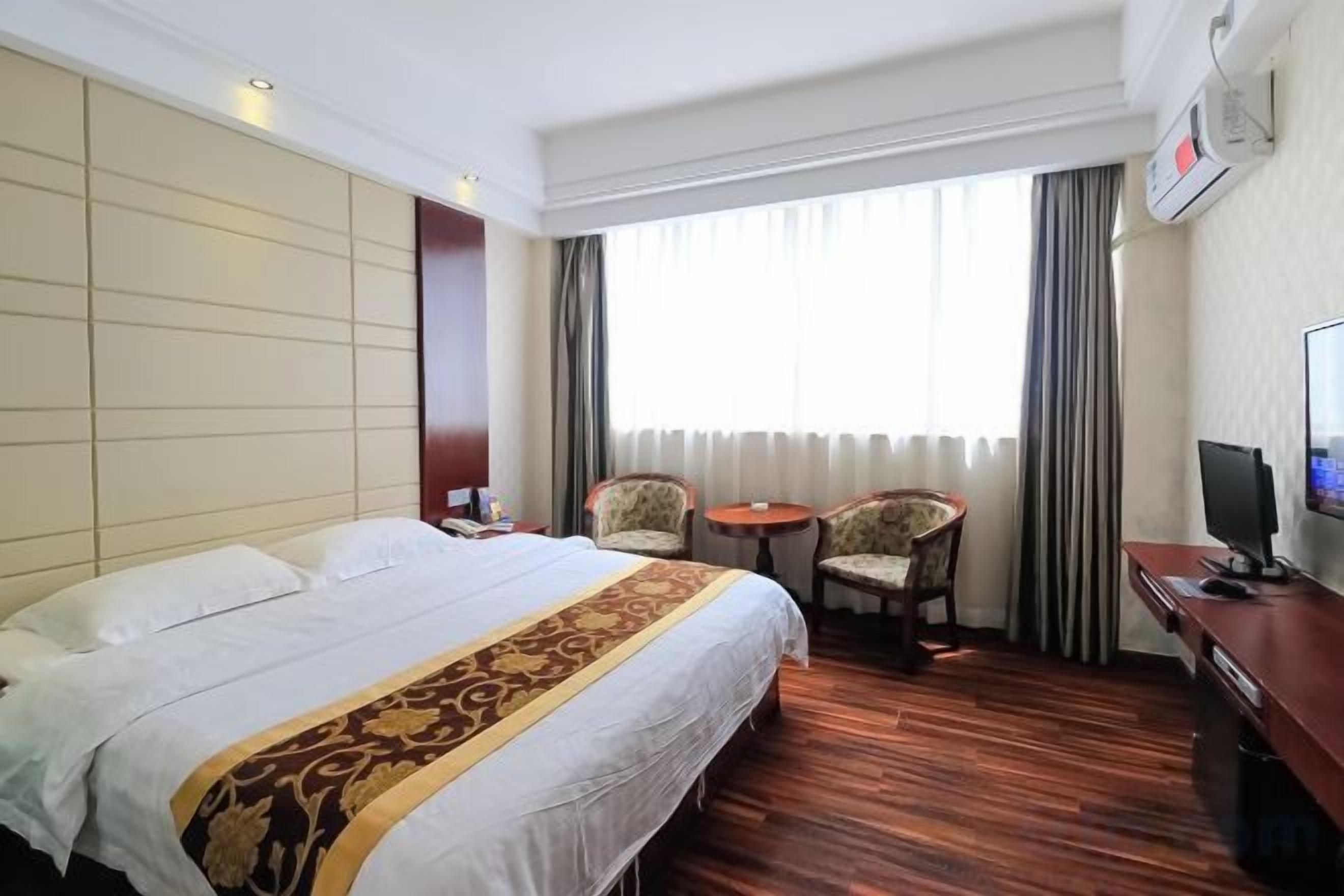 A hotel room with a large bed, a desk with a computer, two chairs, and a TV.