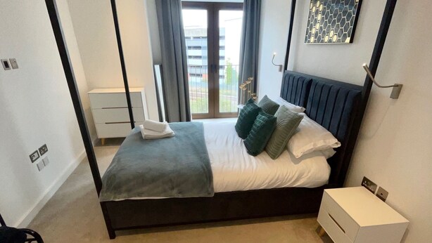 Une chambre à coucher avec un lit à baldaquin, une table de chevet, une œuvre d’art accrochée au mur et une vue à travers une porte vitrée.