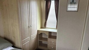 A bedroom with a bed, a wardrobe, a desk with drawers, and a window with curtains. - Caravan situated on Coastfields, Ingoldmells (Skegness)