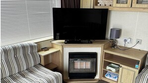 A living room with a flat-screen TV, a striped sofa, a fireplace, and wooden shelves. - Caravan situated on Coastfields, Ingoldmells (Skegness)