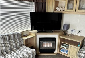 Ein Wohnzimmer mit Flachbildfernseher, einem gestreiften Sofa, einem Kamin und Holzböden.