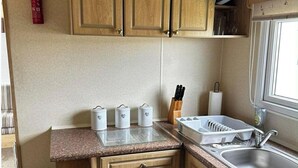 A kitchen with wooden cabinets, a granite countertop, a sink, and a window. - Caravan situated on Coastfields, Ingoldmells (Skegness)