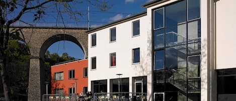 Un bâtiment moderne doté d’une façade en verre, d’une arche en briques et d’un immeuble rouge attenant.