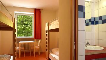 A room with bunk beds, a desk, a chair, and a window with a view of trees.