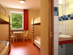 Una habitación con literas, un escritorio, una silla y una ventana con vista a árboles.
