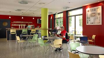 A cafeteria with round tables and chairs, a bar area, and large windows allowing natural light.