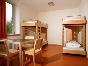 Ein Zimmer mit Etagenbetten, einem Tisch, Stühlen und einem Fenster mit Vorhängen.
