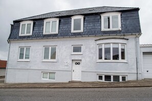 Ein zweistöckiges Gebäude mit weißer Fassade, Hausnummer 12, mit zahlreichen Fenstern und einer mittleren Tür.