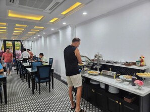 A restaurant with a tiled floor, a buffet counter with food items, and a person serving. - Elegant Hotel (Xuan Huong - Da Lat)