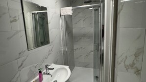 Un baño con ducha de vidrio, lavamanos con espejo y paredes con diseño de mármol.