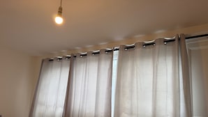 Una habitación con cama, mesita de noche, lámpara y ventana con cortinas.