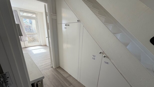 Un pasillo con una escalera, una puerta que da a una habitación y un cartel en la pared.