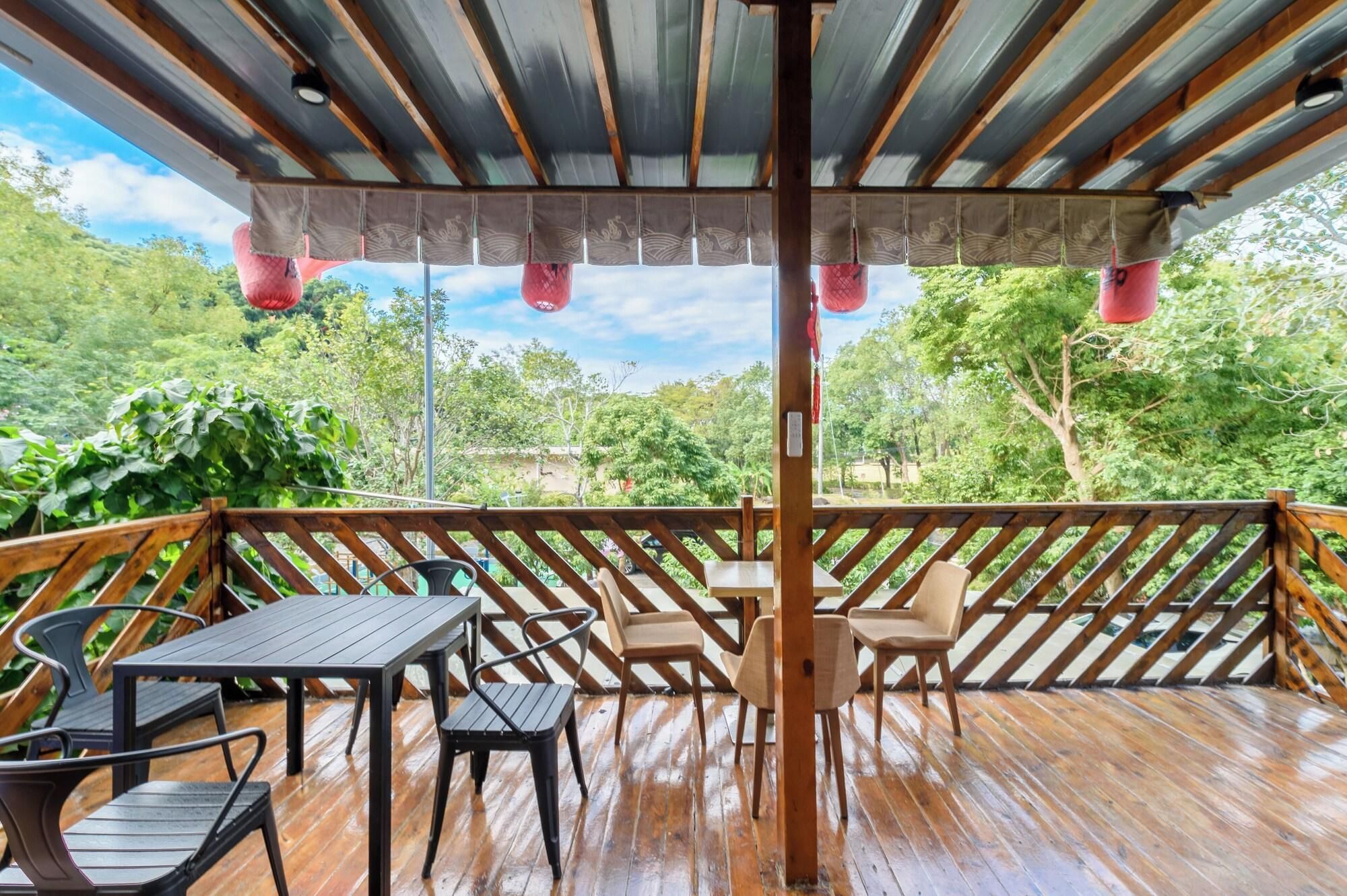 Una terraza de madera con mesas y sillas, una pérgola con cortinas de tela y vistas al follaje.