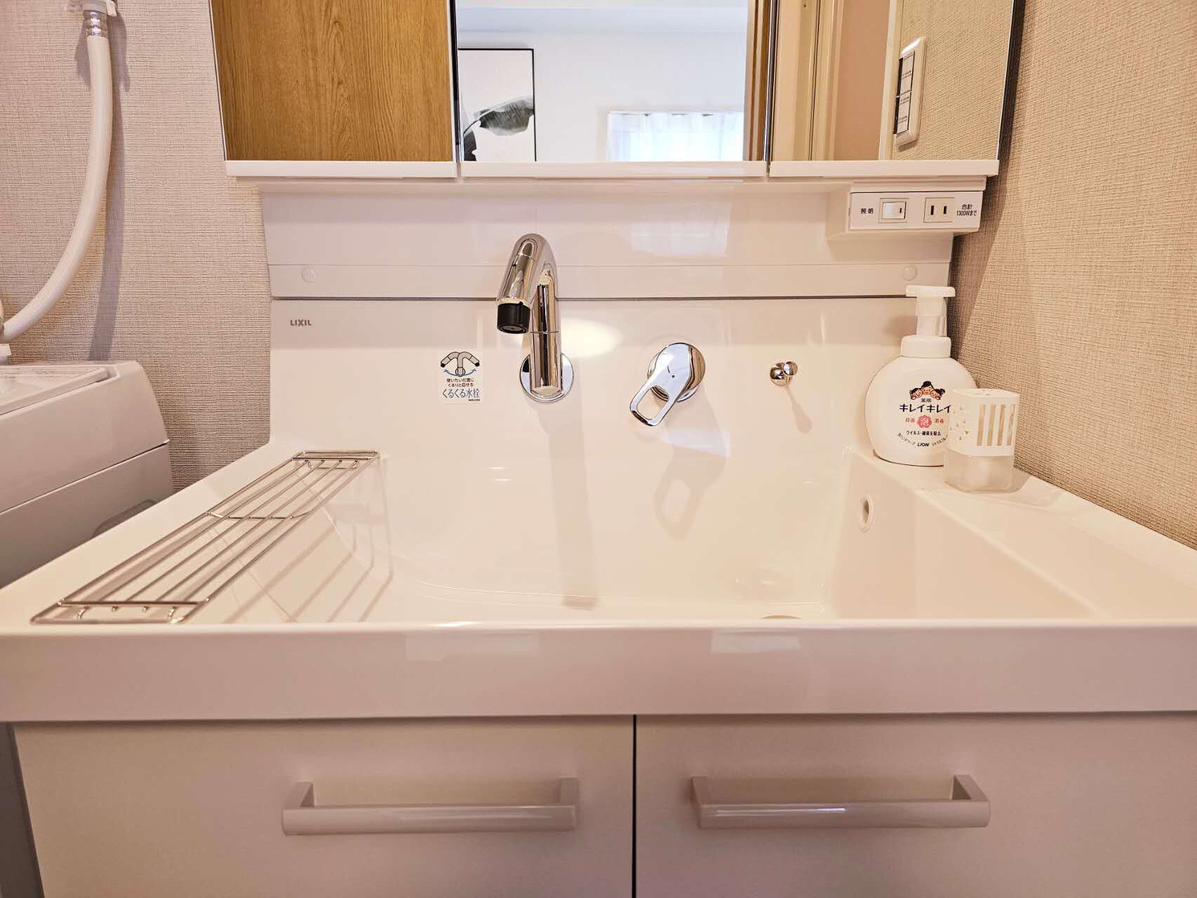 A bathroom with a white sink, chrome faucet, and a mirror above it. There are two small drawers below the sink and a towel rack to the left.