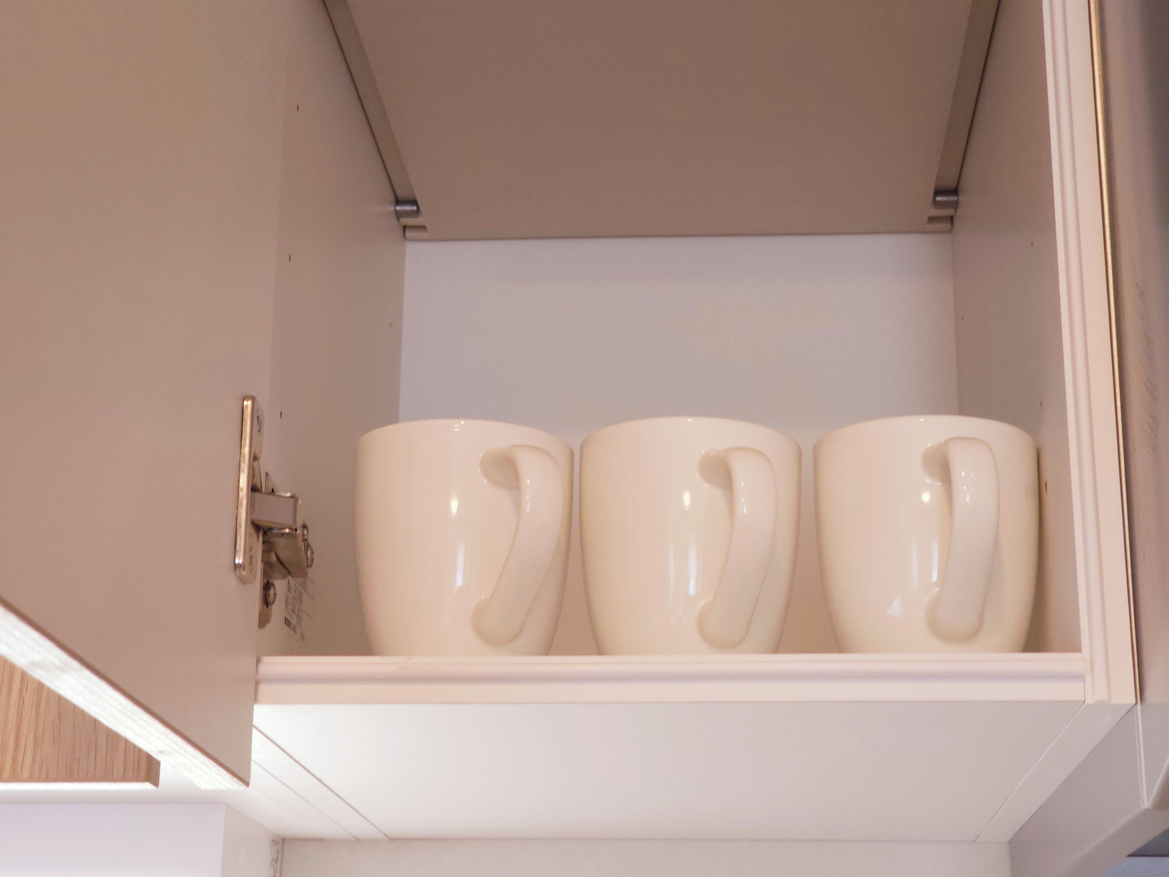 A white shelf with three white ceramic mugs.