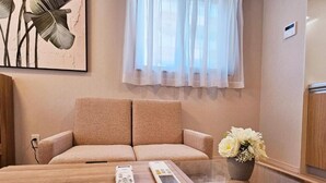 Una habitación con sofá, una mesa de centro de vidrio, un control remoto y un florero con flores.