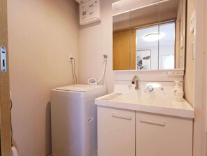 A bathroom with a washing machine, a sink with a mirror, and a shower.