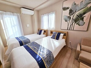 A room with two beds, a sofa, an air conditioner, and a large plant.