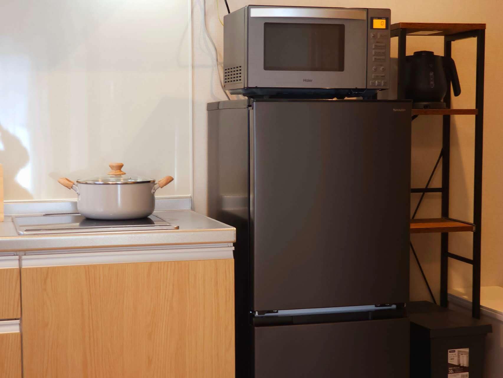 Eine Küche mit einer Mikrowelle auf dem Kühlschrank, einem Topf auf der Arbeitsfläche und einem Regal mit einer Kaffeemaschine.