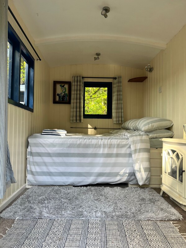 A bedroom with a bed, a window with curtains, a nightstand, and a lamp.
